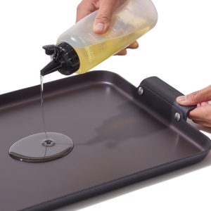 Pouring oil onto the OXO Outdoor double burner griddle after cleaning